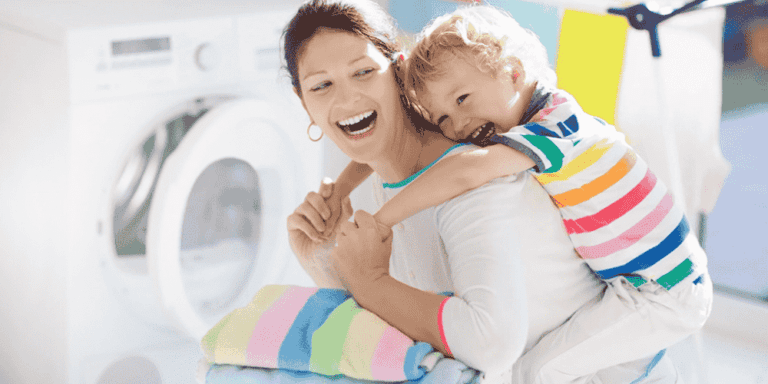 woman and child play in front of a dryer after she folds clean clothes